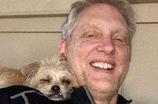 Greg Merritt smiles as his dog perches on his shoulder.