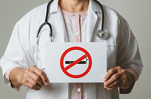 A physician holds a no-smoking sign.