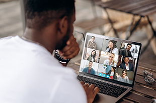 Image depicts a man participating in a virtual meeting on his laptop.