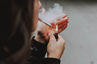 A woman lights a cigarette.