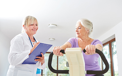 A woman participates in cardiac rehab while a care provider looks on.