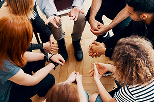 A close up of a group sitting in a circle of chairs.