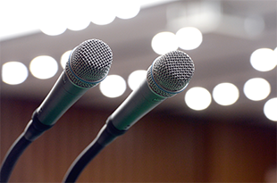 Two metal microphones sit in stands in the foreground. There is bokeh in the background.