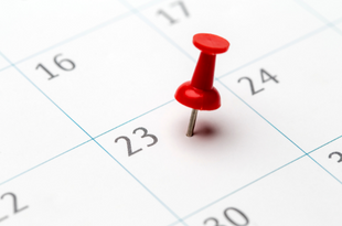 A red thumb tack marks the 23rd day on a close up of a calendar.