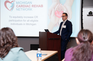 Dr. Mike Thompson presents during the inaugural MiCR Annual Meeting as attendees look on. A slide with the MiCR mission shines from the projector. 