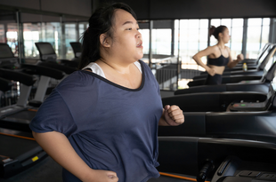 A woman of Asian descent runs on a treadmill. Her hair is back in a ponytail and she is wearing a blue t-shirt.