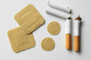 nicotine replacement therapy patches sit on a white background. Next to them, on the right, lay two broken cigarettes.