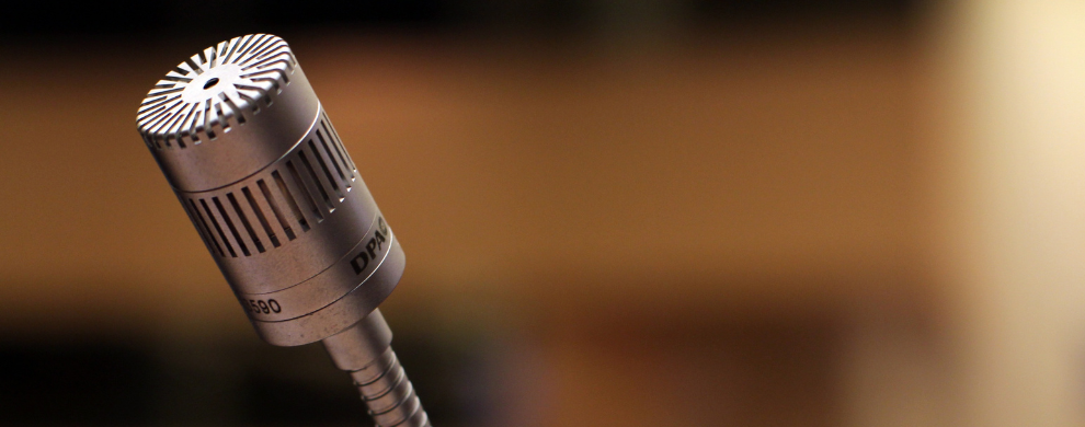 A silver metal microphone is in focus in front of a neutral blurred background.