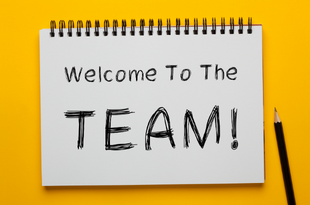 A note pad with the words, "Welcome to the Team!" rests on a bright yellow background with a black pencil sitting to the right.