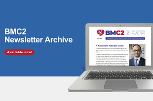An image of a laptop on a white table top with a blue background. The laptop screen displays the BMC2 newsletter, including the BMC2 logo and a welcome note from Dr. Hitinder Gurm with a portrait of him. Dr. Gurm has short dark hair and wears dark glasses, a white button-down dress shirt, and a blue tie with a dark suit jacket. He is smiling.