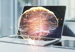 A digital image of a brain is superimposed over a laptop that is sitting on a white table.