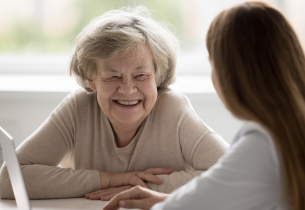 An older female patient smiles while sitting with a female doctor.