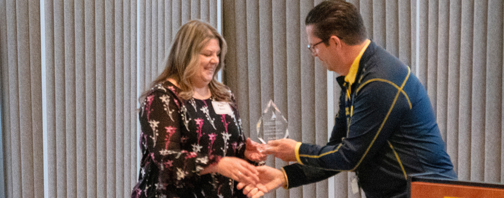Pam Benci stands near a podium receiving the 2026 MHealthy Dr. Robert Winfield Champion Award
